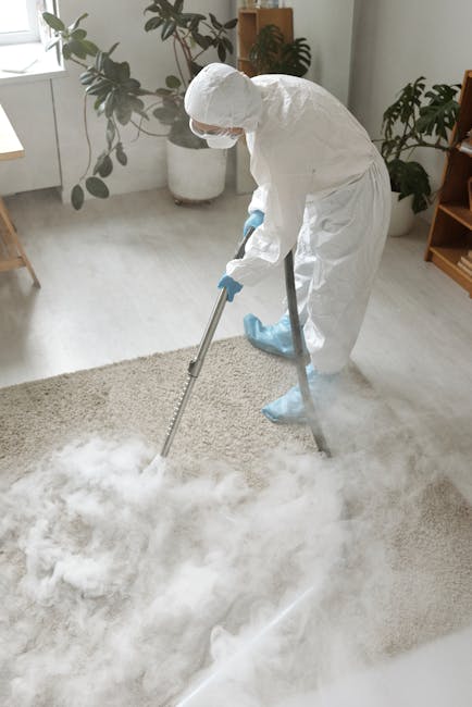 A person kneeling on a patterned carpet in a living room setting, using a yellow and black vacuum cleaner to perform surface cleaning and deep cleaning of the carpet. Their hands are inserting or remo